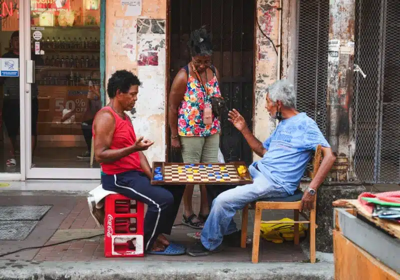 A woman interrupting two men playing chess with bottle caps in Santa Ana neighborhood